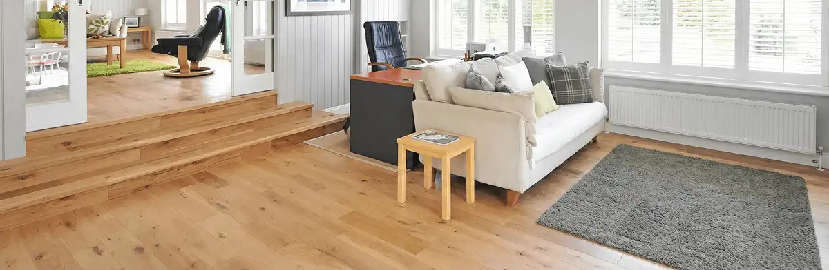 A modern living room with professionally installed laminate flooring, a beige sofa, a small side table, a gray rug, and large windows with white shutters in Milwaukee, WI